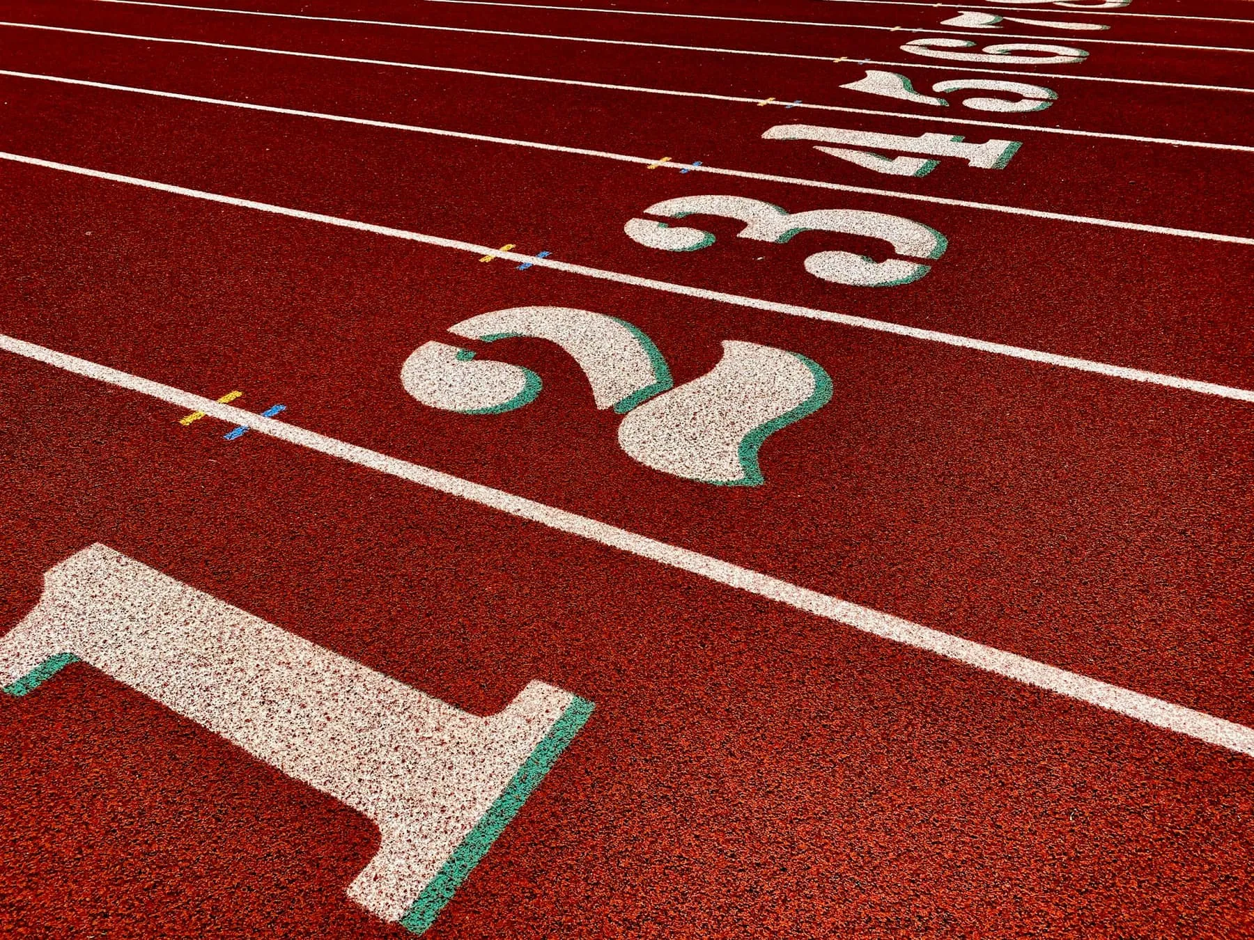 Czerwona bieżnia lekkoatletyczna z namalowanymi numerami torów.