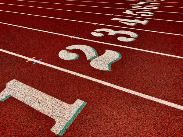 Czerwona bieżnia lekkoatletyczna z namalowanymi numerami torów.