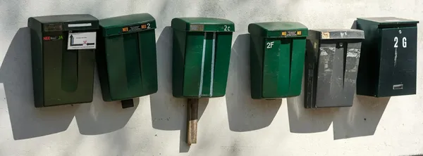 Rząd zielonych skrzynek na listy przymocowanych do jasnej ściany.