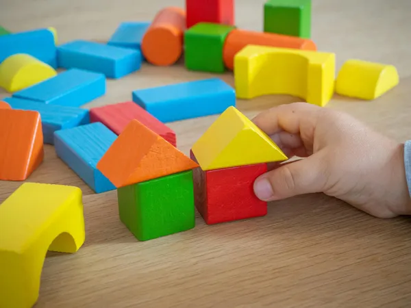 Dziecięca dłoń układająca kolorowe drewniane klocki na stole.