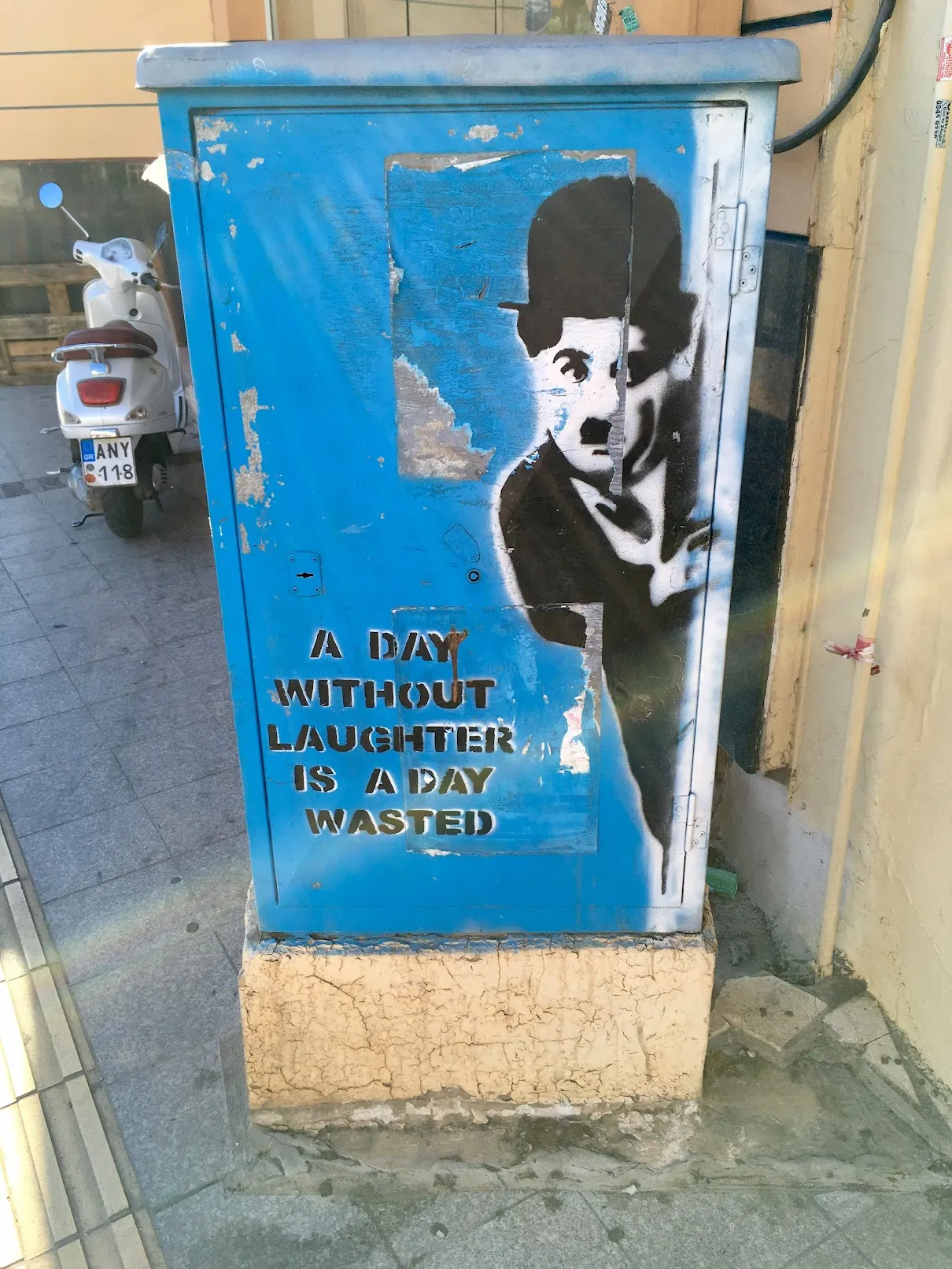 Graffiti on a utility box featuring a black-and-white image of Charlie Chaplin with the quote: 'A day without laughter is a day wasted'.