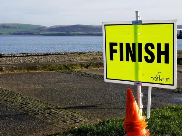 Żółta tablica z napisem FINISH ustawiona przy nadmorskiej promenadzie.