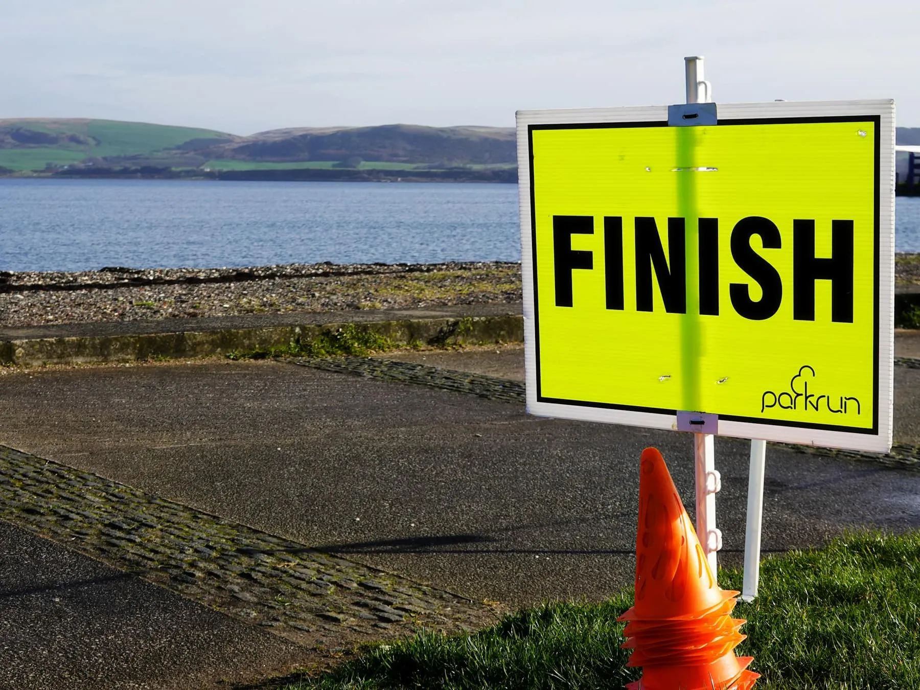 Żółta tablica z napisem FINISH ustawiona przy nadmorskiej promenadzie.