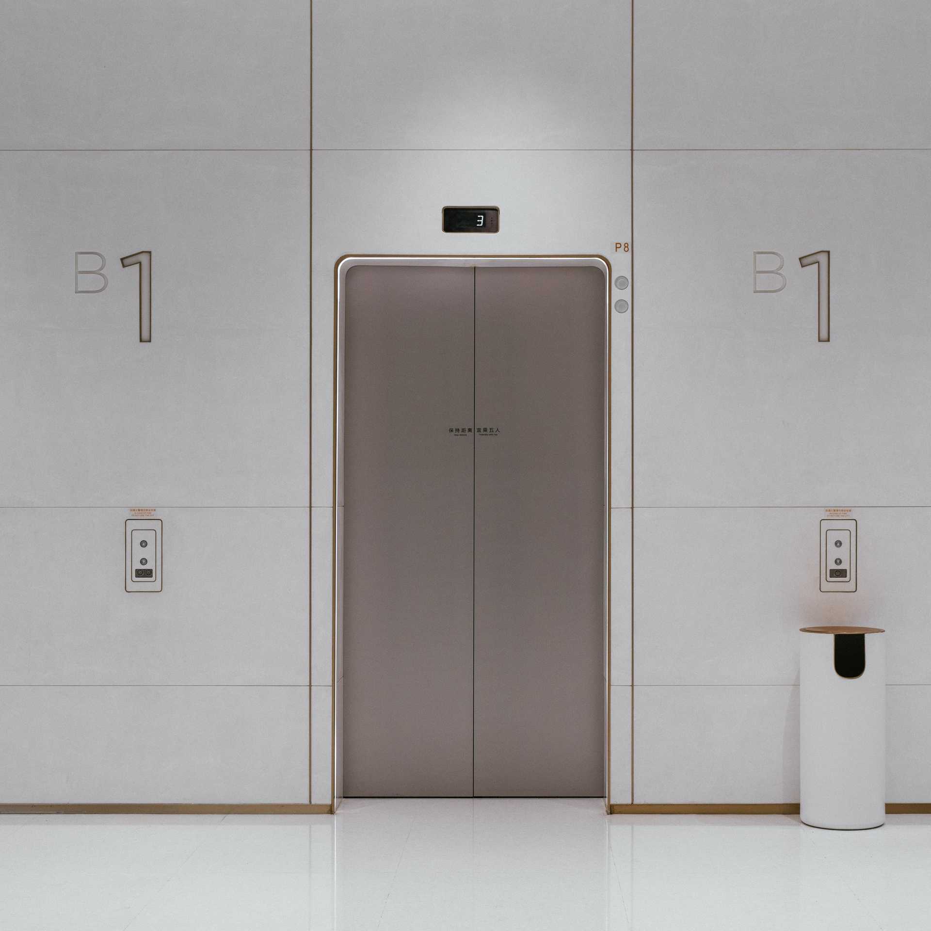 Fotografia eleganckiego wnętrza z białymi ścianami i srebrnymi drzwiami windy. Photo by Edwin Chen on Unsplash.